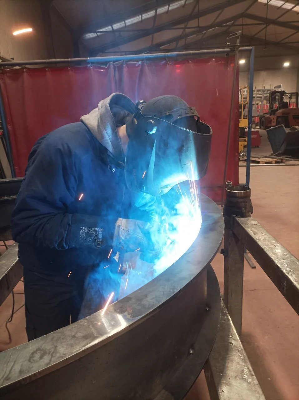 Denys welding a curved metal assembly in the workshop